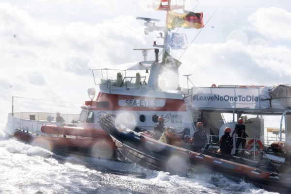 SEA-EYE 5 auf dem Mittelmeer mit RHIB-Beiboot und Crew an Deck, Banner #LeaveNoOneToDie sichtbar