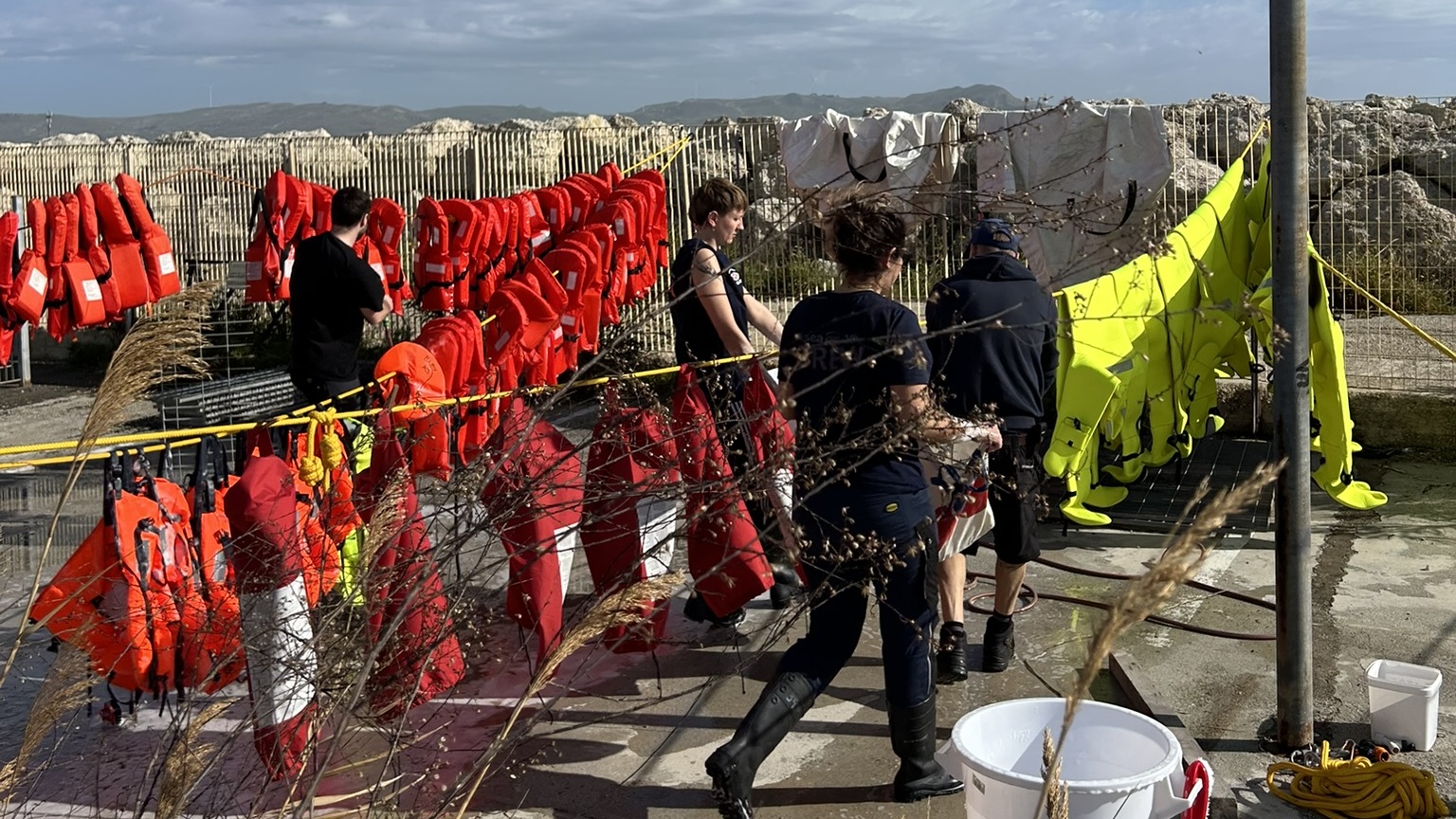 Sea-Eye volunteers clean red life jackets outdoors at the harbor