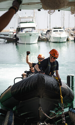 Sea-Eye crew members in helmets maneuver a RHIB in the harbor on board the Sea-Eye 5