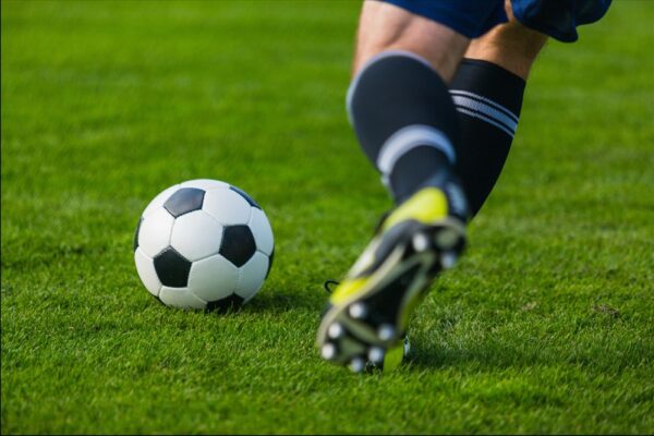 Beine eines Mannes in Fußballoutfit laufen einem Fußball hinterher.