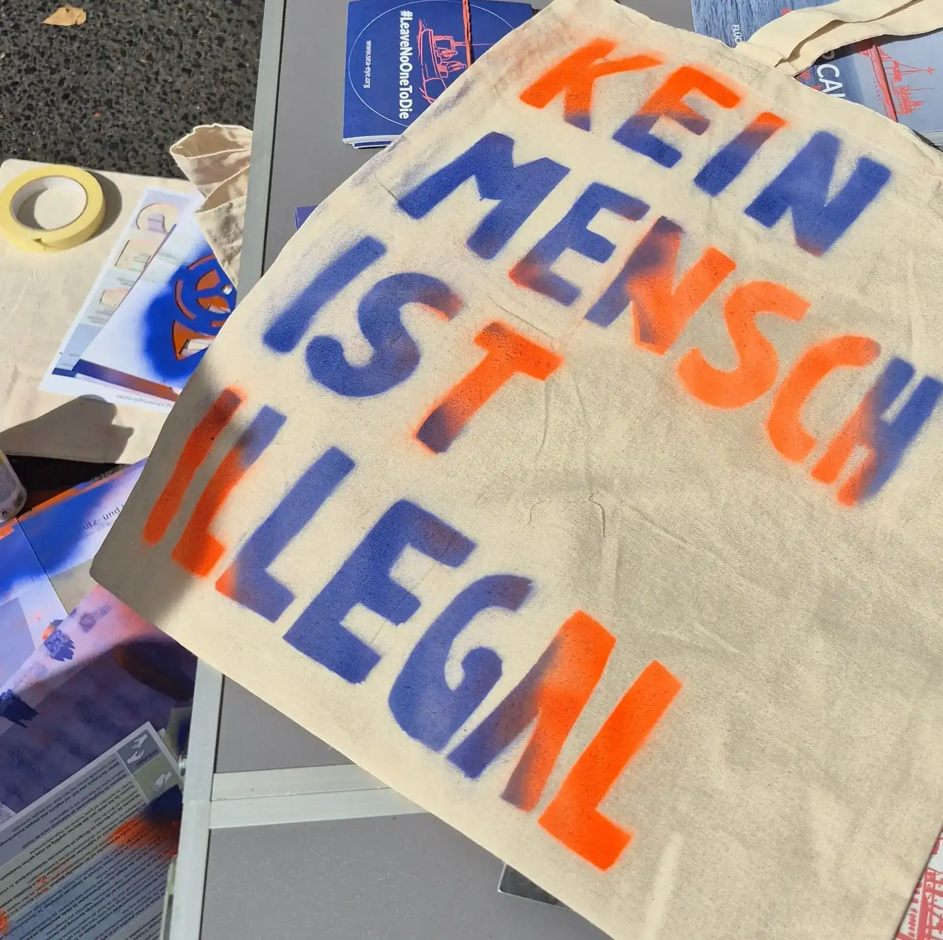 Beutel mit der aufgesprühten Aufschrift 'KEIN MENSCH IST ILLEGAL' auf einem Stand bei einem Straßenfest in Düsseldorf