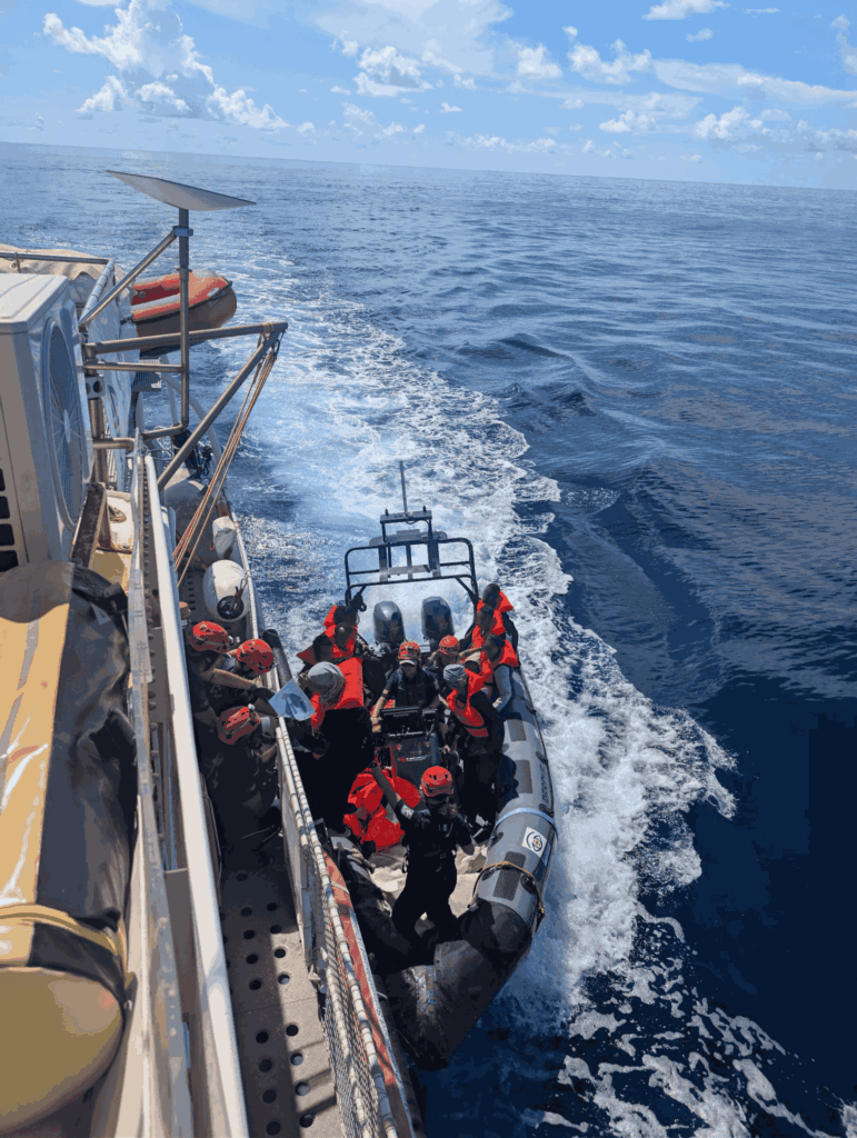RHIB mit Crew und Überlebenden an Bord fährt neben Rettungsschiff auf offenem Meer
